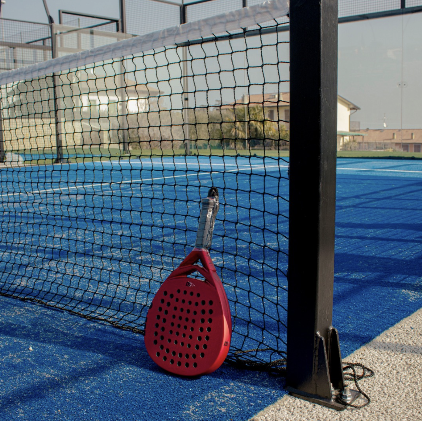 Racchetta padel appoggiata alla rete del campo